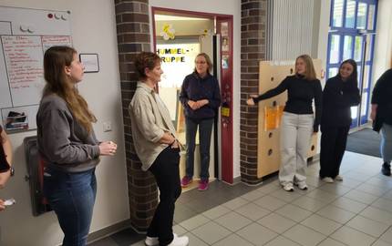 Drei Kolleginnen aus der Kita Rathausstraße führen die Krippenkräfte durch die Einrichtung. Auf dem Bild stehen die Kräfte im Flurbereich und gucken sich die Aushänge an.