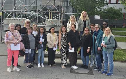 Die Teilnehmenden stehen vor dem Messeeingang. Es ist ein Gruppenbild. Sie stehen zusammen im Halbkreis.