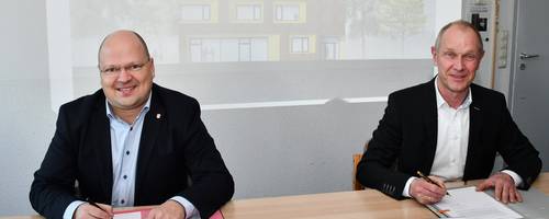 Der Bürgermeister und der Generalunternehmer sitzen an einem Tisch und unterzeichnen einen Vertrag.