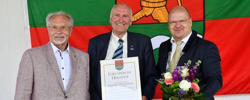 Drei Herren vor dem Wappen Laatzens mit Urkunde und Blumenstrauß.