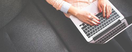 Eine Frau sitzt auf einem Sofa und schreibt am Laptop.