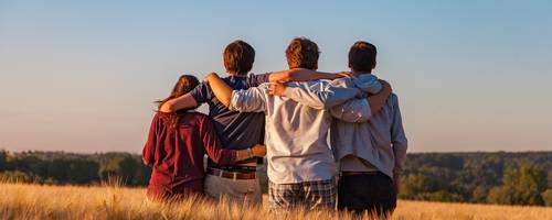 Gruppe Jugendlicher sitzt auf einer Wiese. Alle haben sich gegenseitig die Arme um die Schultern gelegt.