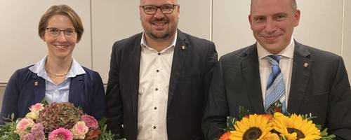 Der Bürgermeister überreicht seiner Vertreterin und dem zukünftigen Stadtrat jeweils Blumensträuße.