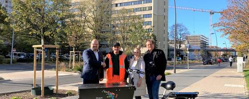 Vier Menschen vor einem Lastenrad. Im Hintergrund ist eine Straße mit Brücke zu sehen.