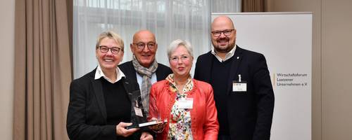 Eine Gruppe von zwei Frauen und zwei Männern stehen in einem Raum vor einem weißen Vorhang.