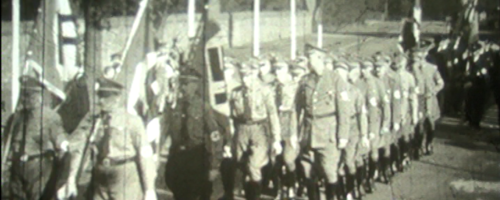 schwarz weiß Aufnahme von einer Reihe Männer in NS Uniformen, die marschieren.
