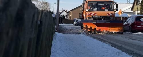 Ein LKW mit einem Schneeschild schiebt Schnee auf einer verschneiten Fahrbahn zur Seite.