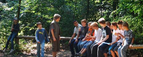 Eine Gruppe Jugendlicher sitzt im Wald auf einem Holzbalken