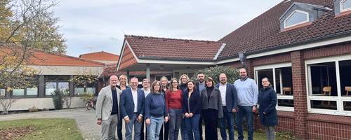 14 Personen stehen vor dem Eingang eines Schulgebäudes.