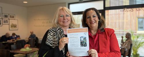 Zwei Frauen stehen nebeneinander und halten einen Ausdruck des Newsletters in die Kamera.