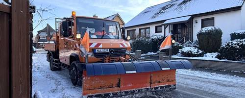Ein Räumfahrzeug mit breitem Schneeschild fährt über eine verschneite Straße.