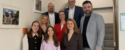 Fünf Frauen stehen neben drei Männern auf einer Treppe. Alle lächeln in die Kamera.