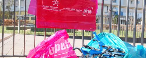 Einige rote Mülltüten und Müllzangen liegen an einem Metallzaun.