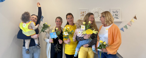 Fünf Frauen stehen gut gelaunt nebeneinander. Zwei von ihnen haben ein Kleinkind auf dem Arm.