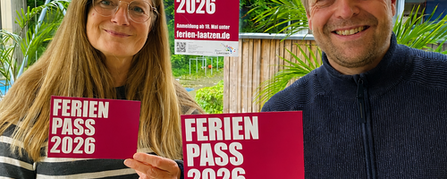 Eine Mitarbeiterin und ein Mitarbeiter des Kinder- und Jugendbüros halten Flyer mit dem Programm des Ferienpasses in die Kamera.