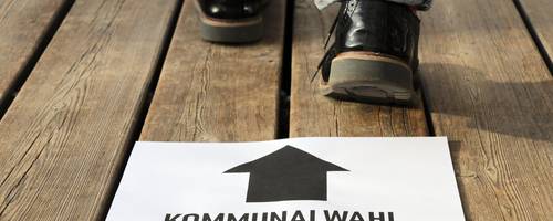 Ein weißes Blatt Papier mit der Aufschrift Kommunalwahl und Füsse, die dahinter stehen.