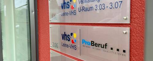 Eine rote Wand mit Hinweisschildern der Leine VHS.