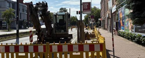 Gelbe Baustellenbaken sperren eine Baustelle ab, auf der bereits ein Bagger steht.