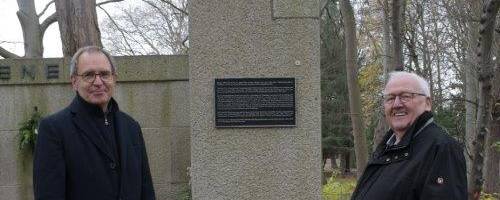 Bürgermeister Köhne und Ortsbürgermeister Stuckenberg stehen vor der Erklärtafel am alten Ehrenmal