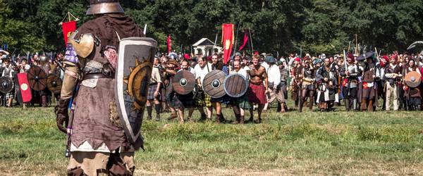 Mittelalterlich verkleideter Kämpfer steht mit einem Schild bewaffnet einer Gruppe auf einem Feld gegenüber
