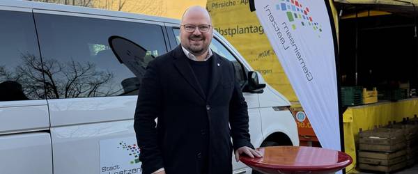 Ein Mann steht auf einem Platz neben einer Beachflag und einem Stehtisch.