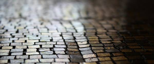 Weg aus Pflastersteinen in der Nacht. Es spiegelt sich das Licht einer Laterne auf den nassen Steinen.