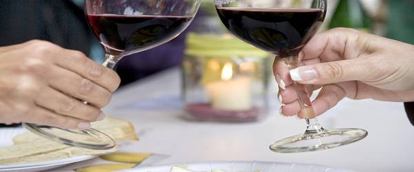 zuprostende Gläser mit Rotwein und Käseplatte im Vordergrund