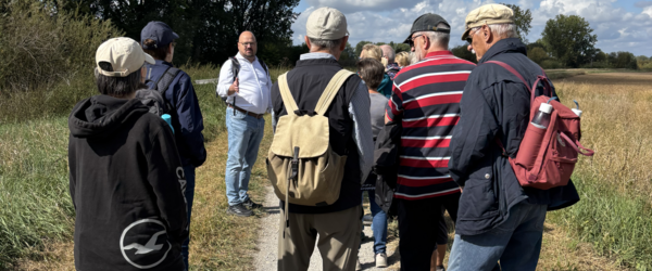 Bürgermeister Kai Eggert spricht auf einem Feldweg zu Personen, die Rucksäcke tragen.