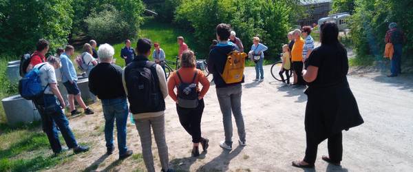 Eine Gruppe von Personen stehend im Kreis, die sich unterhalten. Im Hintergrund grüne Büsche und Gras.