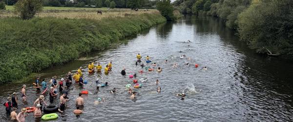 Schwimmerinnen und Schwimmer befinden sich in einem Fluss. Sie sind von oben, von einer Brücke aus fotografiert worden.