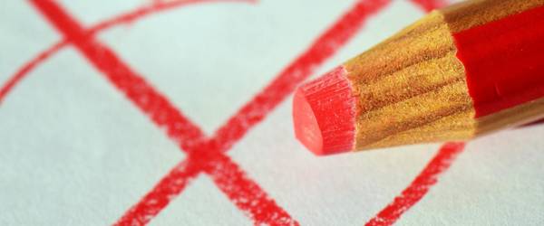 Roter Stift der ein rotes Kreuz gemalt hat. Dieses ist im Hintergund zu sehen.