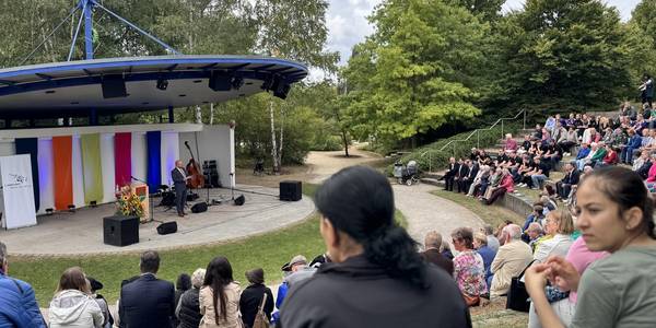 Blick auf die Kulturbühne im Park der Sinne. Bürgermeister Kai Eggert spricht. Viele Personen sitzen im Publikum.